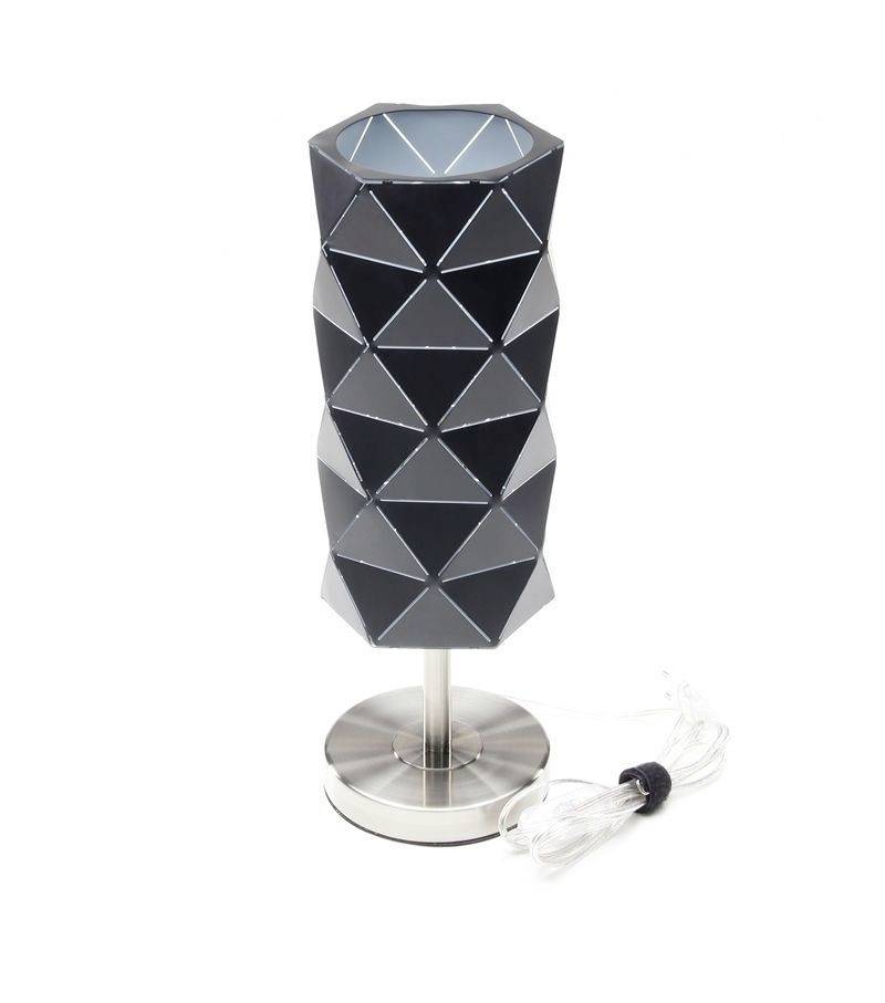 Eine moderne Tischlampe mit einem schwarz-silbernen, geometrischen Schirm auf einem silbernen Metallständer und einem transparenten Kabel.
