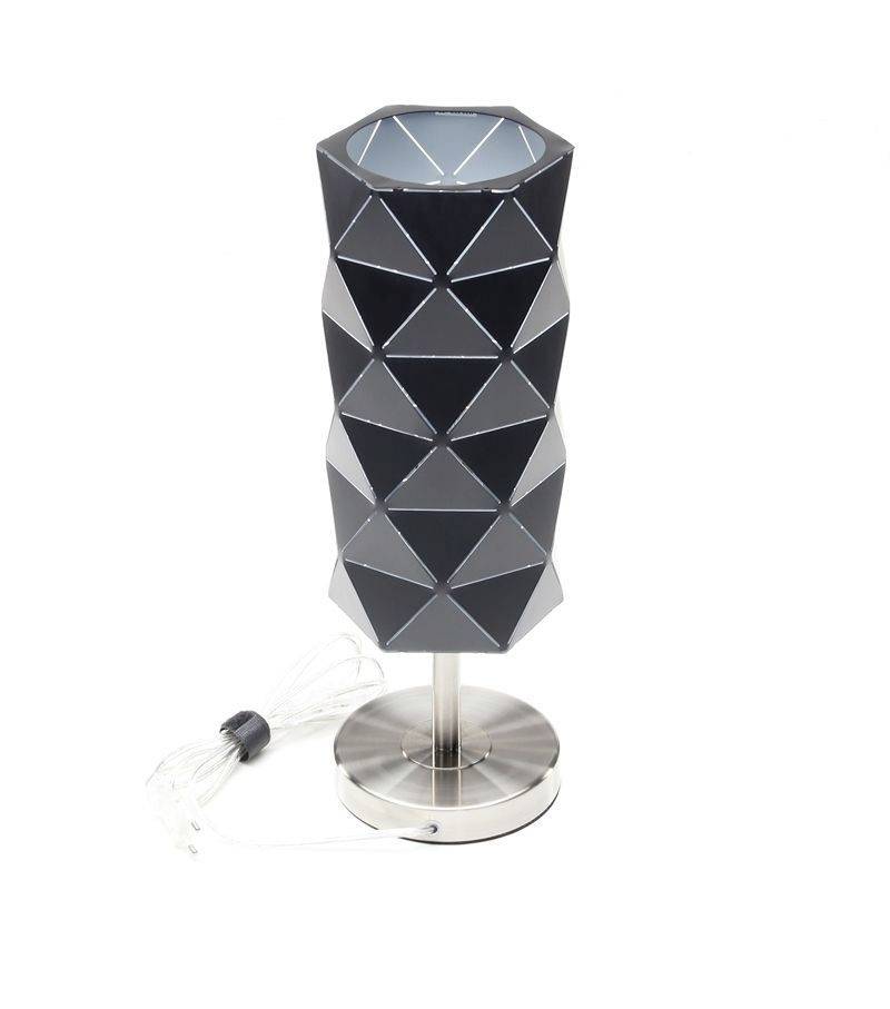 Eine Tischlampe mit einem geometrischen, schwarzen Schirm und silbernem Standfuß, daneben liegt das weiße Stromkabel.