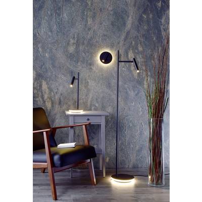 Moderner Wohnbereich mit einem schwarzen Sessel, einem grauen Beistelltisch mit Lampe und einer Stehlampe vor einer strukturierten Wand.
