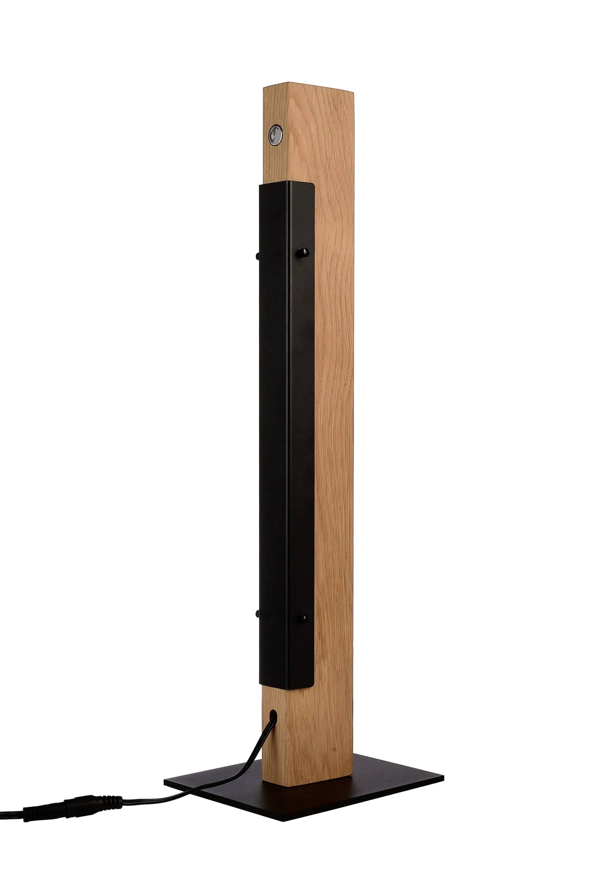 Eine moderne Holzstehlampe mit einem schwarzen Metallelement und quadratischem Sockel. Ein Kabel ist an der Rückseite angeschlossen.