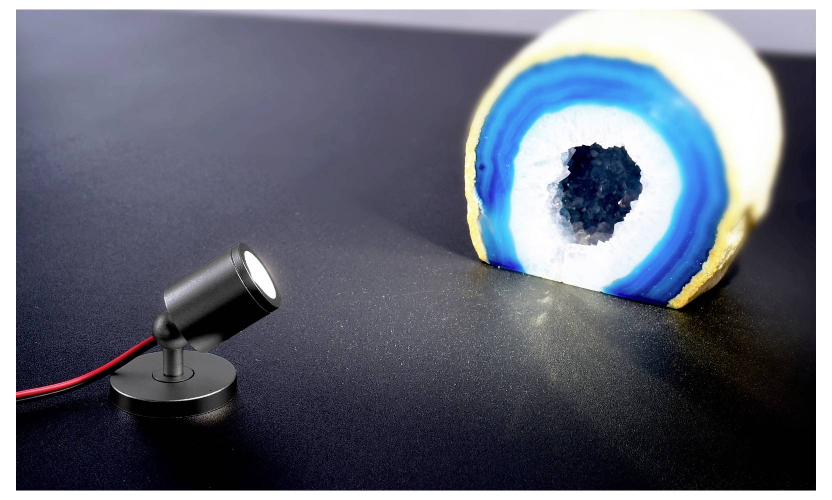 Ein kleiner Scheinwerfer beleuchtet einen aufgeschnittenen Geode und enthüllt blaue und weiße Kristallringe auf einer dunklen Oberfläche.