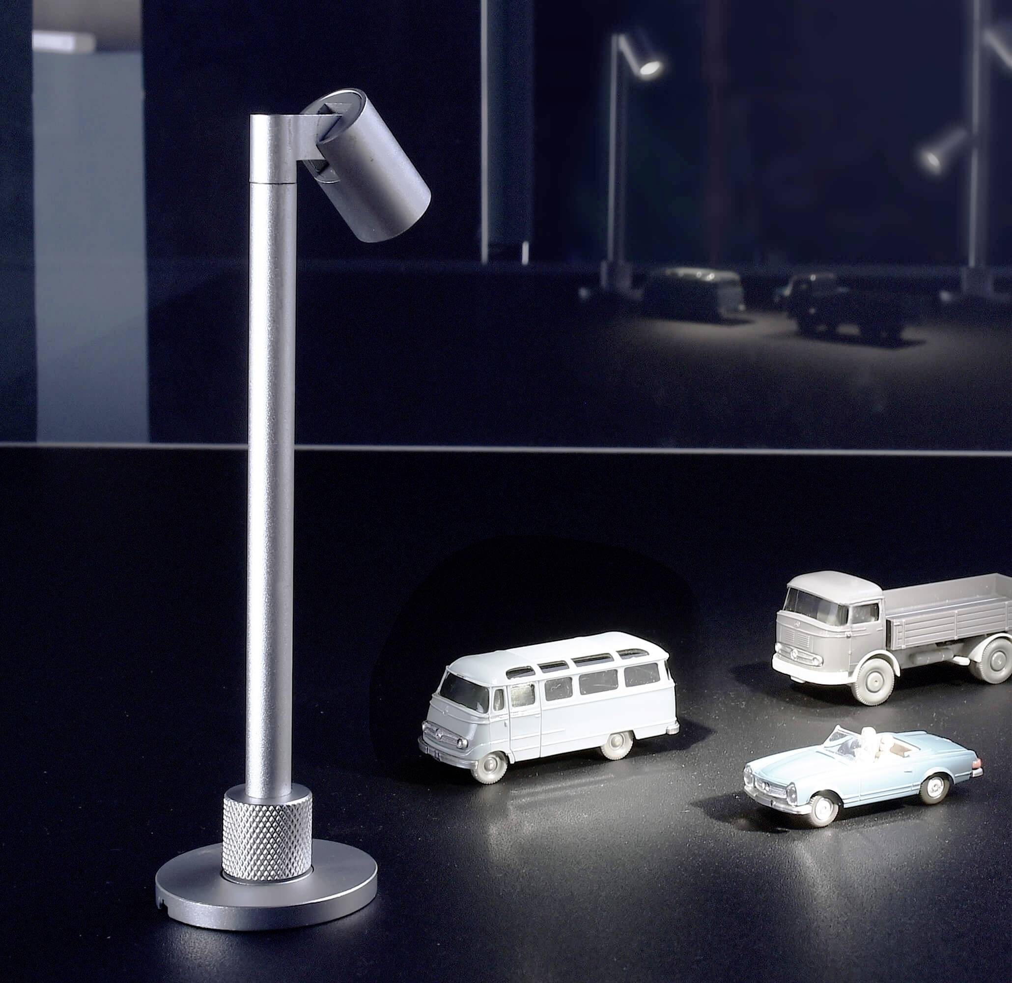 Ein Miniaturmodell zeigt einen beleuchteten Van und zwei Autos. Daneben steht eine moderne Lampe. Im Hintergrund unscharfe andere Autos.