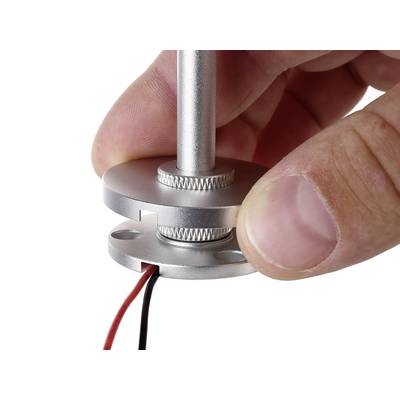 Eine Hand hält eine kleine, runde Metallhalterung mit einer vertikalen Stange und zwei herausragenden Drähten.