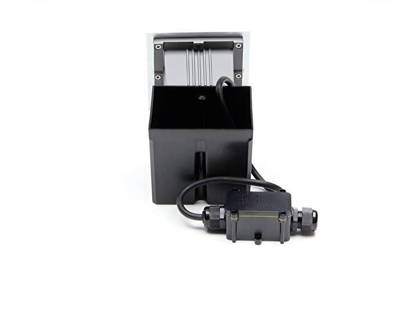 Ein schwarzer elektrischer Adapter mit Kabel, direkt vor einer weißen Wand liegend, Fokus auf die Steckverbindung.