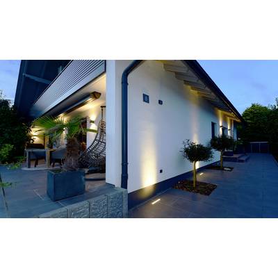 Modernes Haus bei Dämmerung mit stilvoller Außenbeleuchtung. Terrasse mit Hängesessel und Pflanzen an der Seite des Gebäudes.