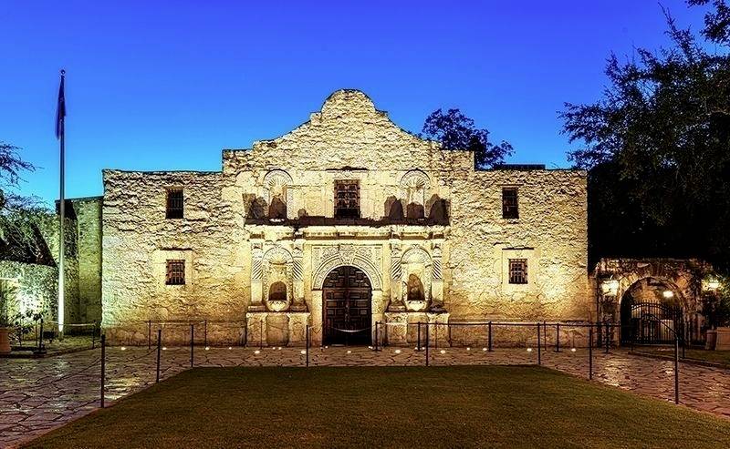 Das Alamo-Gebäude bei Nacht, beleuchtet vor einem tiefblauen Himmel. Historische Architektur mit Steinmauern und dekorativen Details.