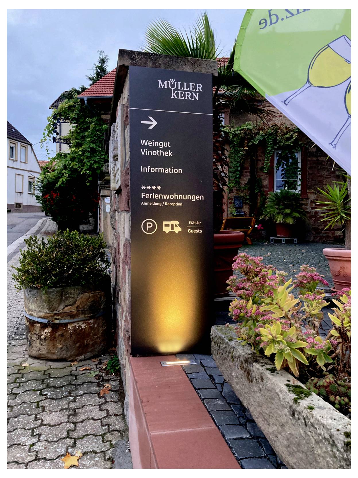 Außenschild mit der Aufschrift „MÜLLER KERN“, das am Gareneingang zum Weinladen, zur Weinbar, zur Information und zu den Ferienwohnungen weist.