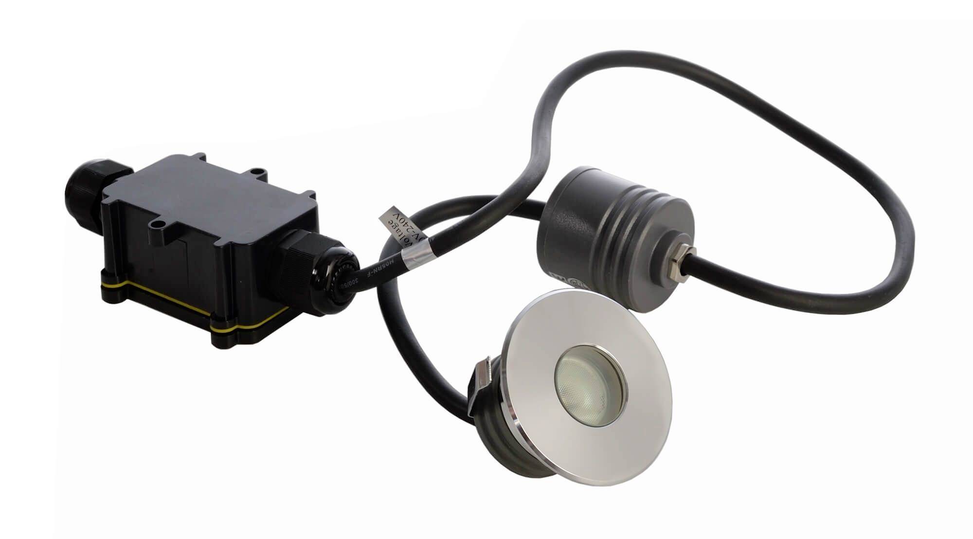 LED-Leuchte mit rundem, silbernem Gehäuse und schwarzem Kabel, verbunden mit einem rechteckigen, schwarzen Anschlusskasten.