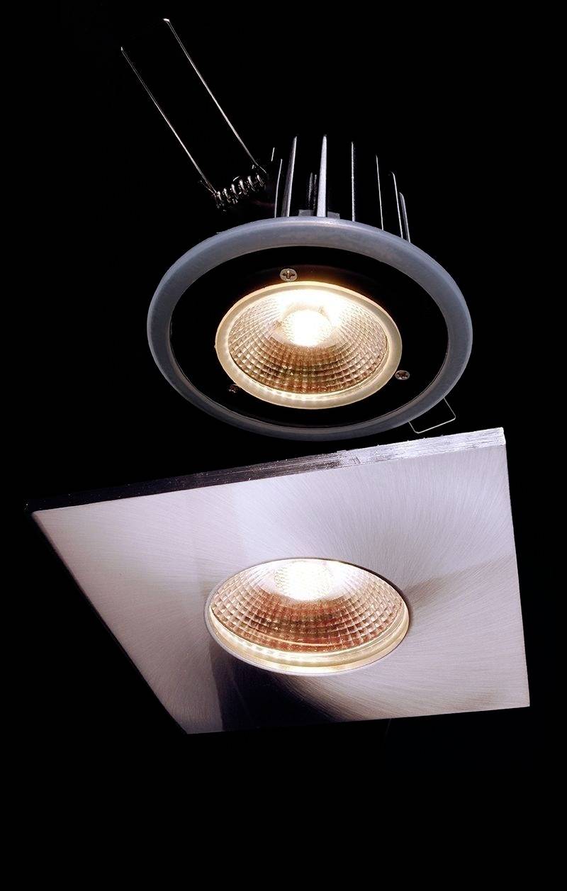 Zwei Einbaustrahler mit Metallrahmen und warmweißer Beleuchtung, die von oben und in einem Winkel sichtbar sind.