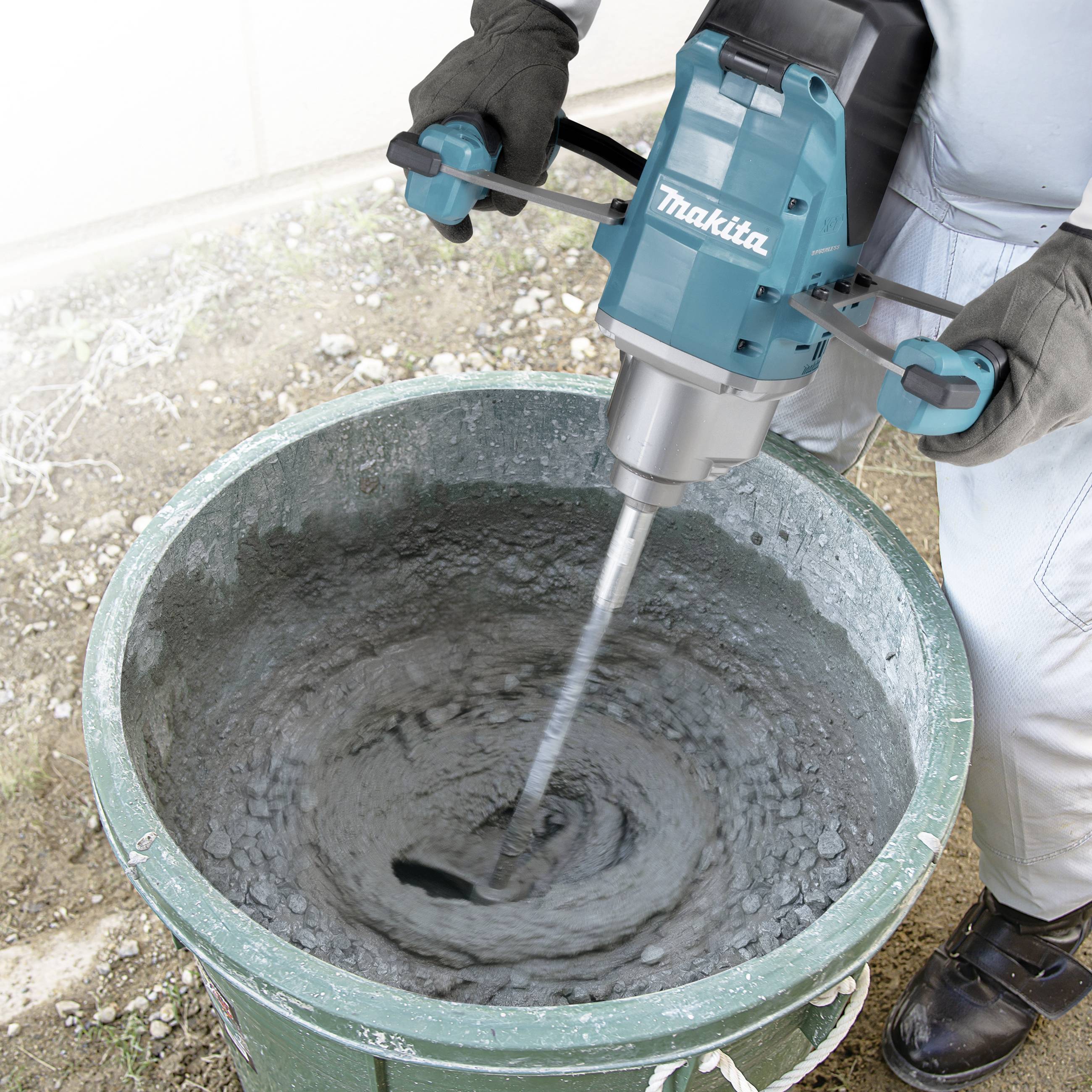 Eine Person mischt mit einem elektrischen Rührgerät Beton in einem Eimer. Schutzhandschuhe werden getragen.