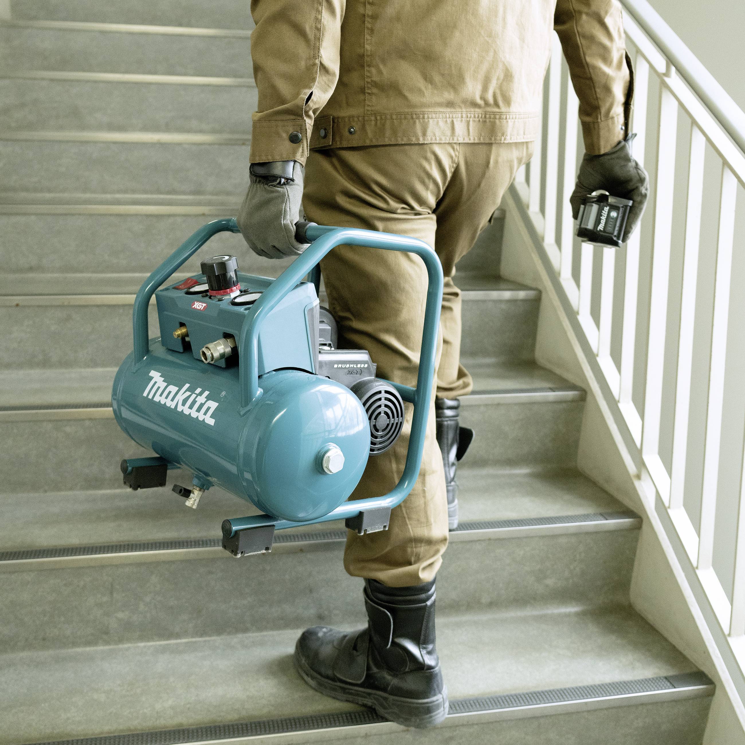Eine Person trägt einen blauen tragbaren Luftkompressor eine Treppe hinauf. Der Kompressor hat die Aufschrift 'Makita'.