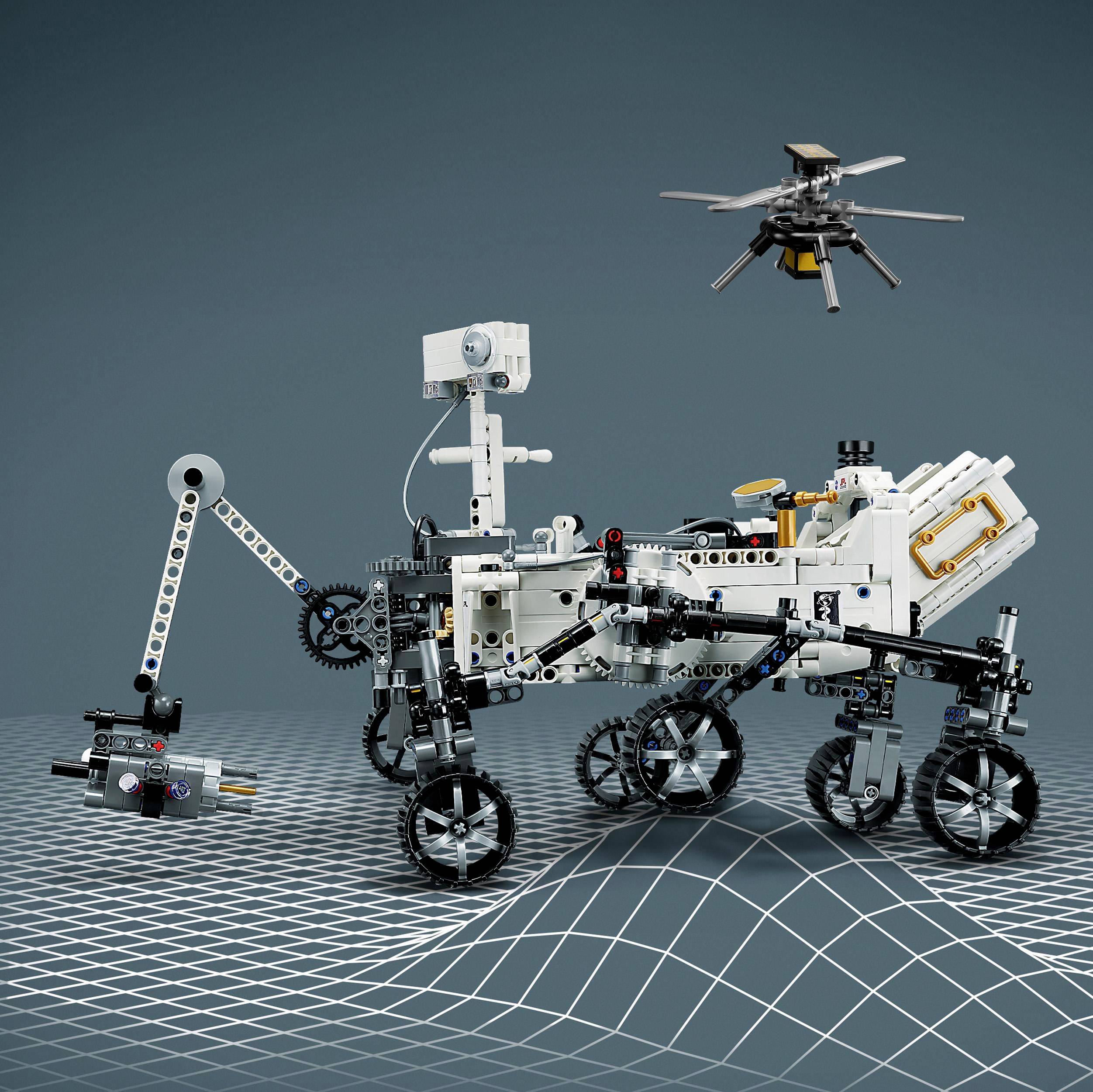 Ein aus Lego gebauter Mars-Rover auf einem gerasterten Boden. Ein kleiner Drohne-ähnlicher Flugroboter schwebt darüber.