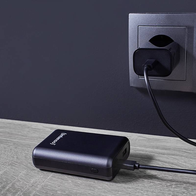 Eine schwarze Powerbank ist mit einem Ladekabel an eine Wandsteckdose angeschlossen. Sie liegt auf einer Holzoberfläche.