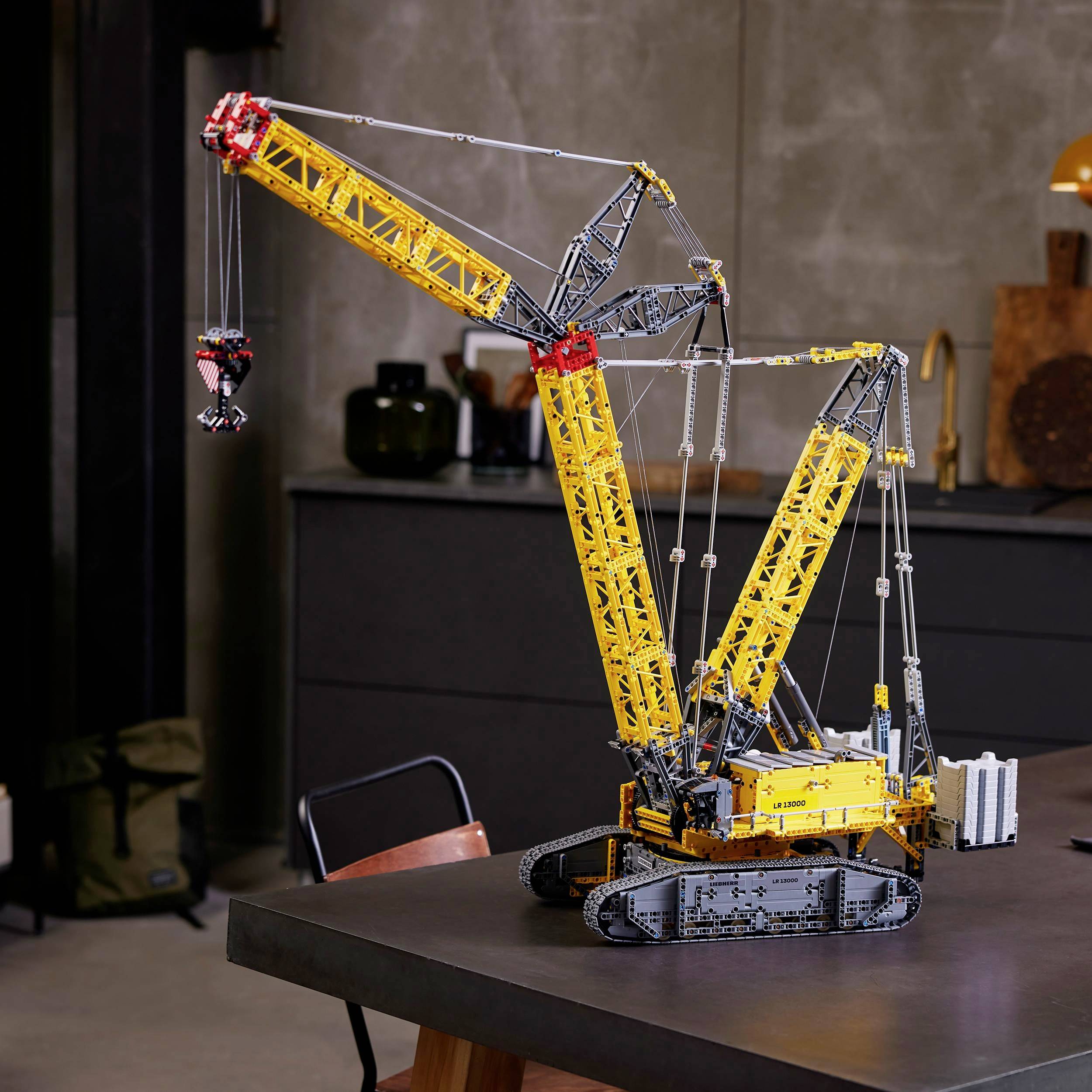 Lego-Kranmodell auf einem Tisch in einem modernen Raum. Der Kran hebt einen kleinen Gegenstand an seinem Haken.