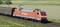 Ein roter Güterzug der DB Cargo fährt auf Schienen durch ländliche Umgebung bei Tageslicht. Links im Bild befindet sich ein Güterwaggon.