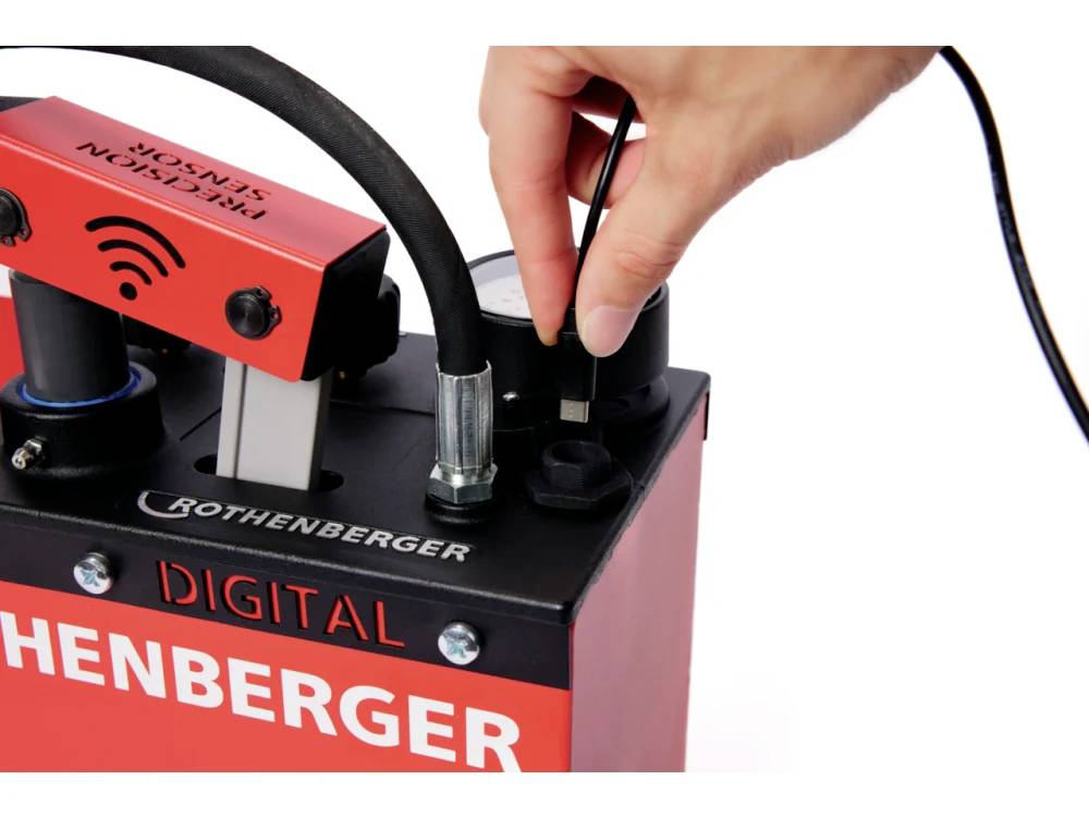 Eine Person justiert ein digitales Messgerät von einer roten Maschine, die mit 'ROTHENBERGER DIGITAL' beschriftet ist. Ein Sensor wird angeschlossen.