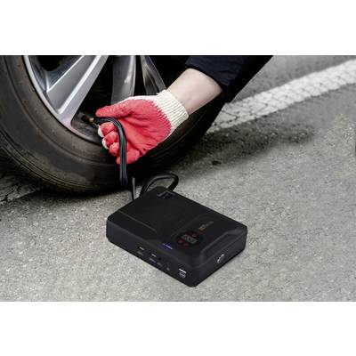 Eine Hand mit roten Handschuhen pumpt Luft in einen Autoreifen mit einem tragbaren Kompressor auf einer Straße auf.