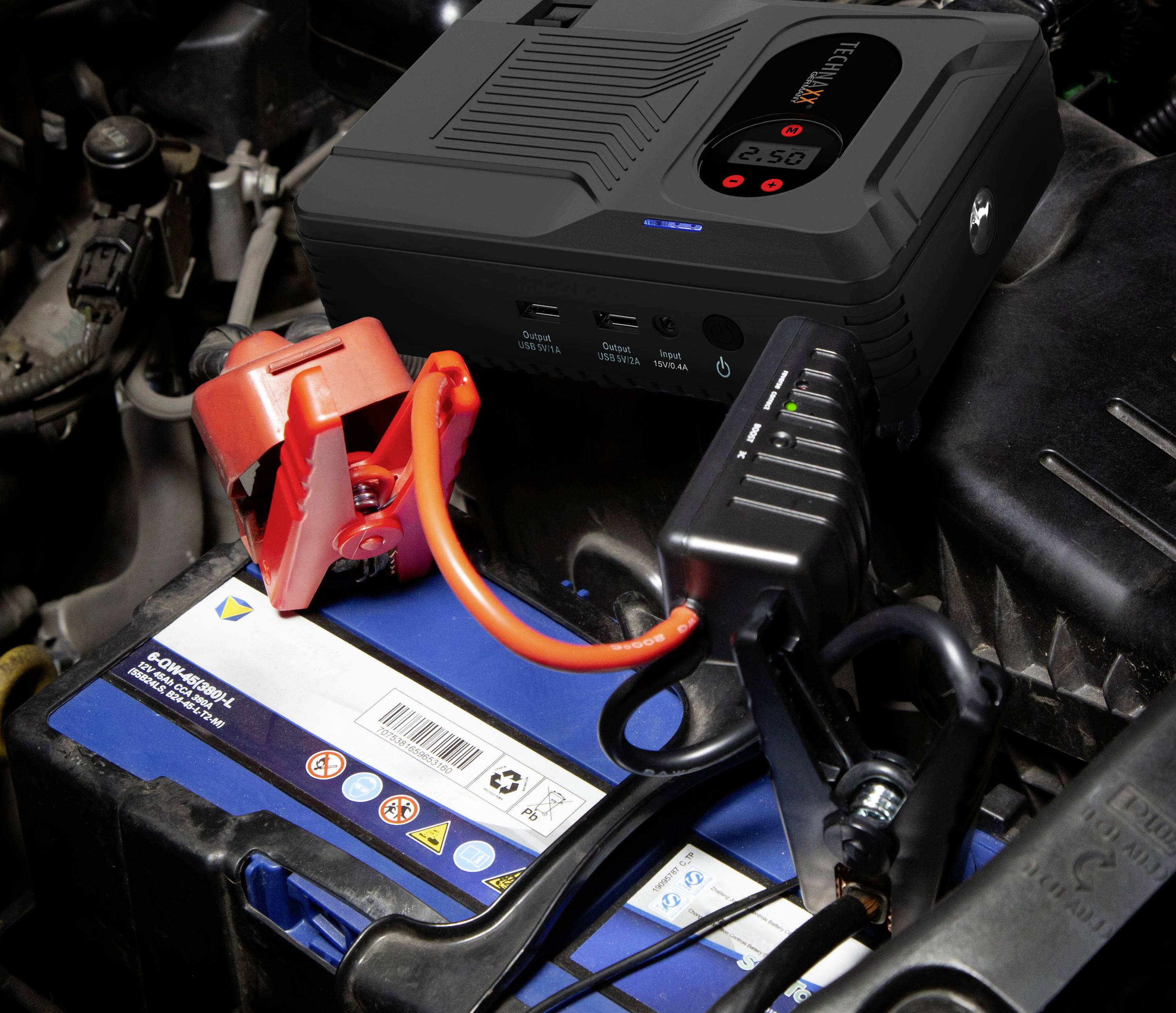 Ein Starthilfegerät ist mit einer Autobatterie verbunden. Die Klemmen sind richtig angebracht: Rot an Pluspol, Schwarz an Minuspol.
