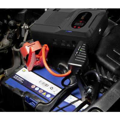Ein Starthilfegerät ist mit einer Autobatterie verbunden. Die Klemmen sind richtig angebracht: Rot an Pluspol, Schwarz an Minuspol.