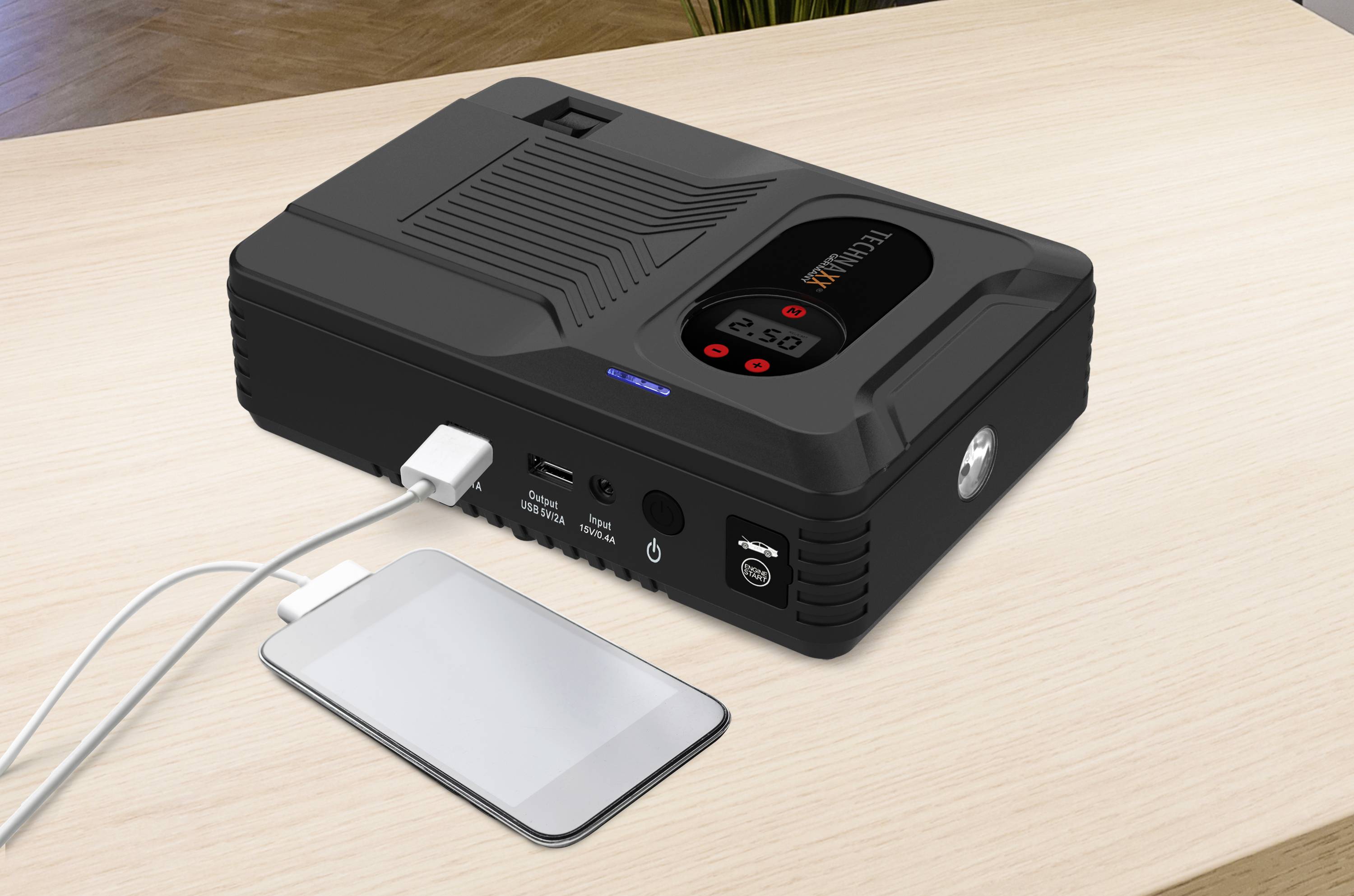 Eine tragbare Powerbank mit mehreren Anschlüssen auf einem Tisch. Ein Smartphone ist über ein Kabel verbunden und wird geladen.