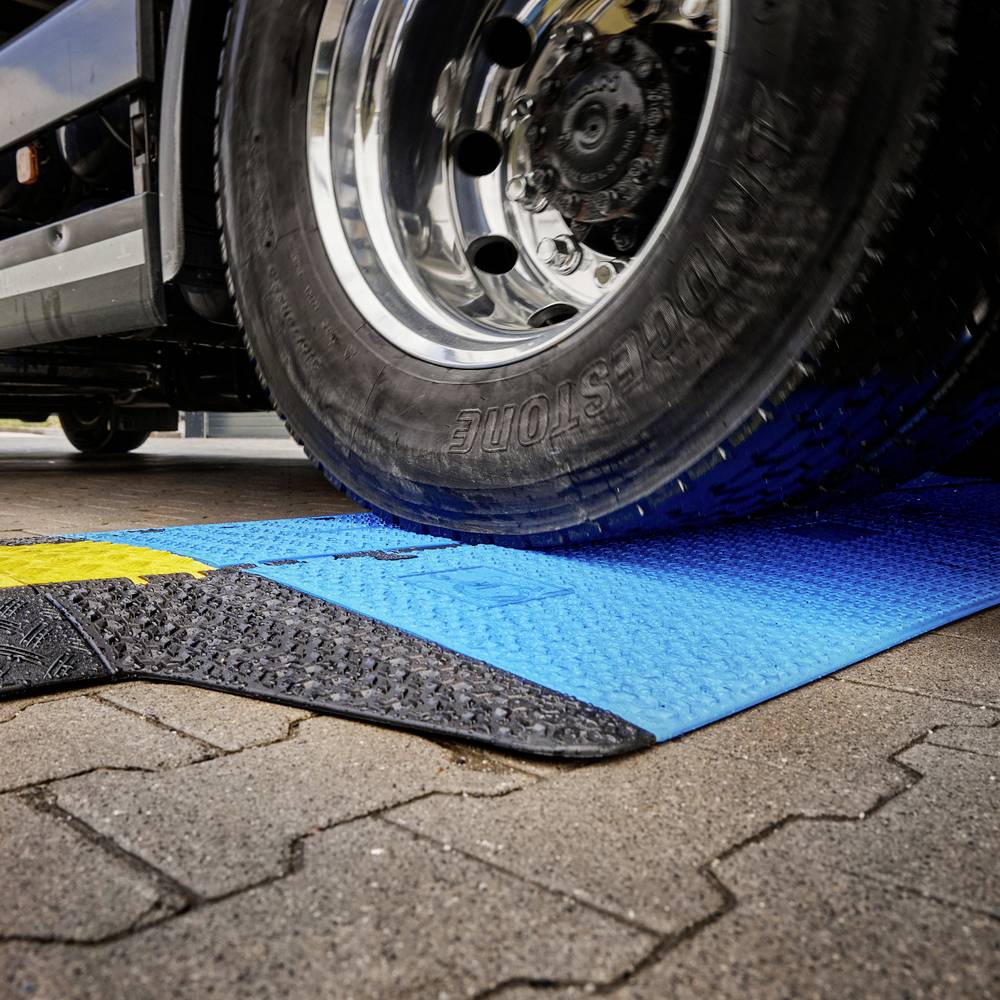 Lkw-Reifen rollt über eine blaue Rampe auf gepflastertem Boden. Rampenstruktur sorgt für Traktion und Stabilität.