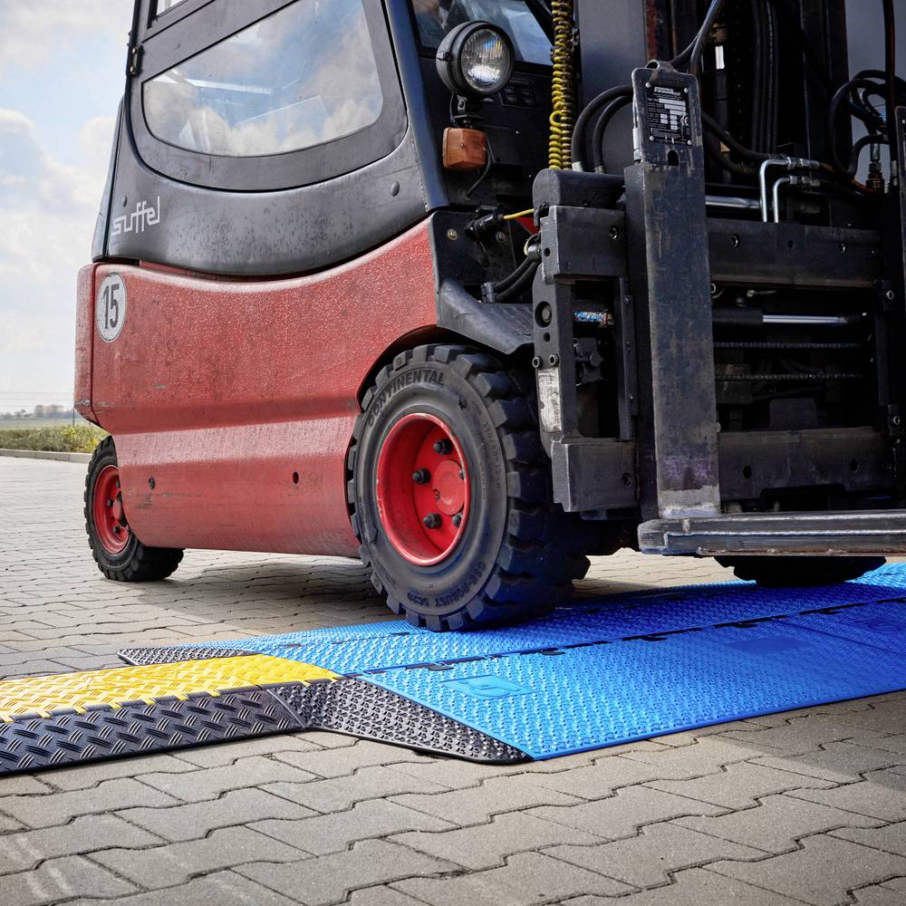 Ein roter Gabelstapler fährt über eine flexible Rampe auf Kopfsteinpflaster. Die Rampe hat gelbe, blaue und schwarze Segmente.