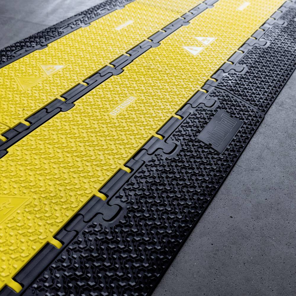 Gummimatten mit schwarzen und gelben Abschnitten auf einem grauen Boden, verbunden durch längliche Kanten; Verwendung in Industrieumgebungen.