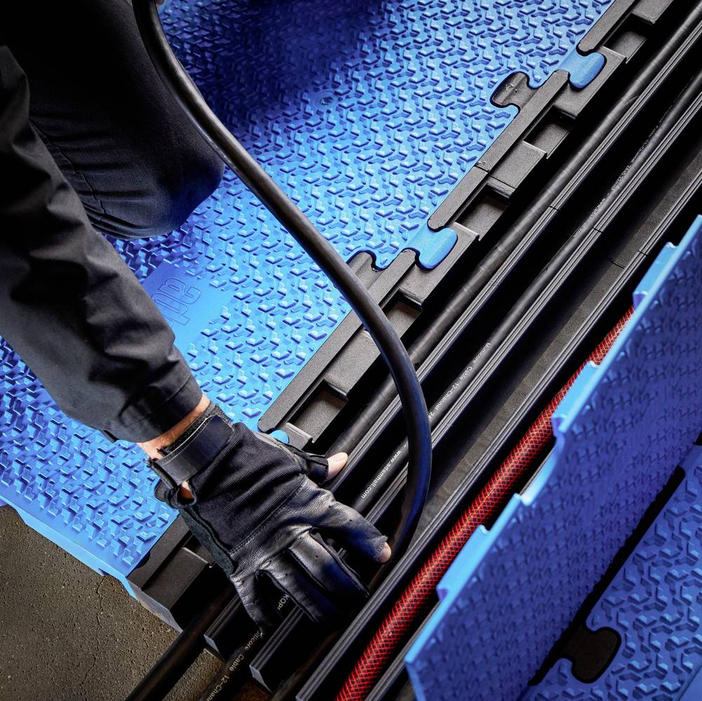 Eine Person in Handschuhen verlegt Kabel in einer blauen, strukturierten Kabelabdeckung auf einem Boden.