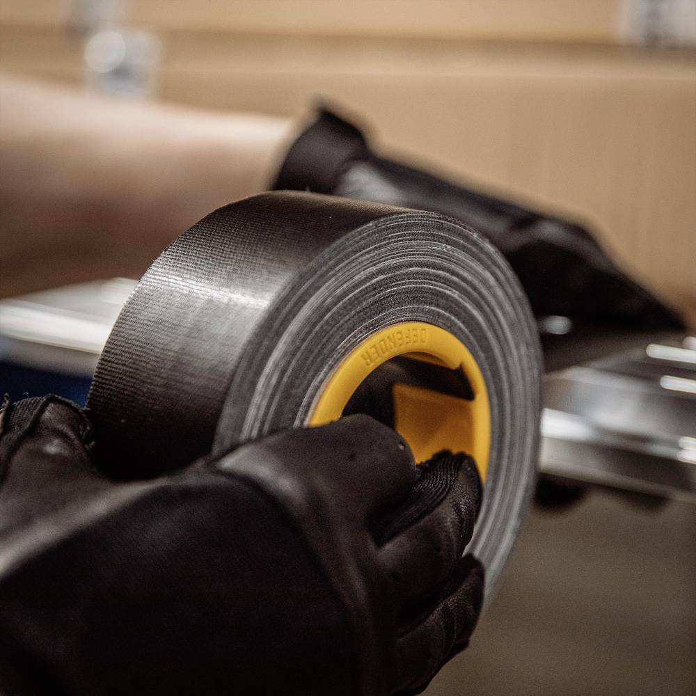 Eine Person hält eine Rolle silbernes Klebeband über einem Tisch und bereitet es zum Einsatz vor.