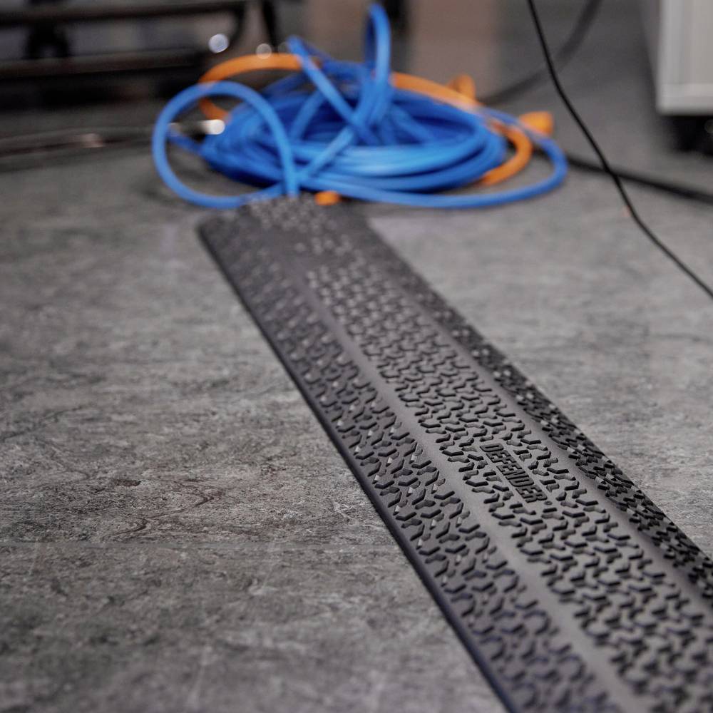 Ein schwarzer Kabelkanal erstreckt sich diagonal über den Boden, daneben liegen orange und blaue Kabel lose zusammengewickelt.