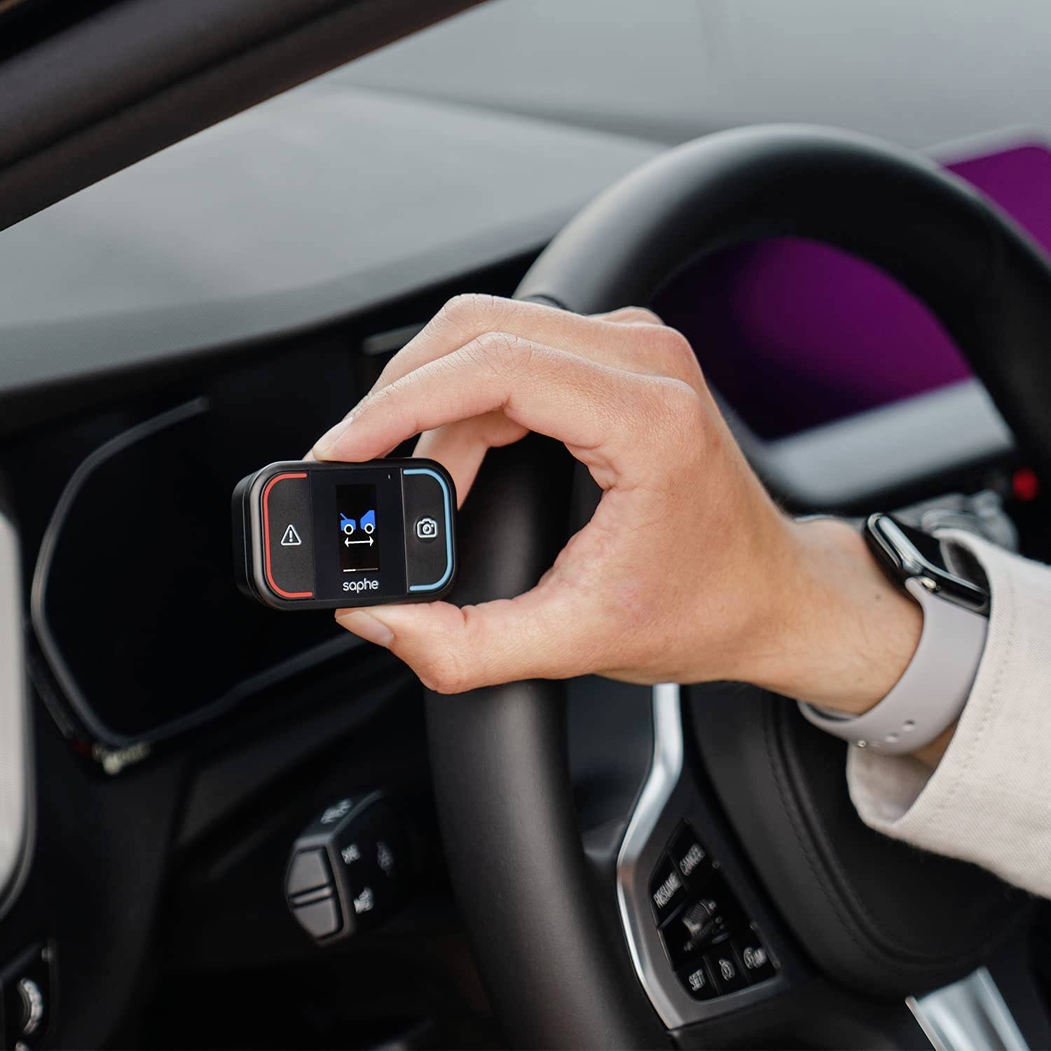 Eine Person hält ein kleines elektronisches Gerät mit Tasten in der Hand. Sie sitzt am Steuer eines Autos.