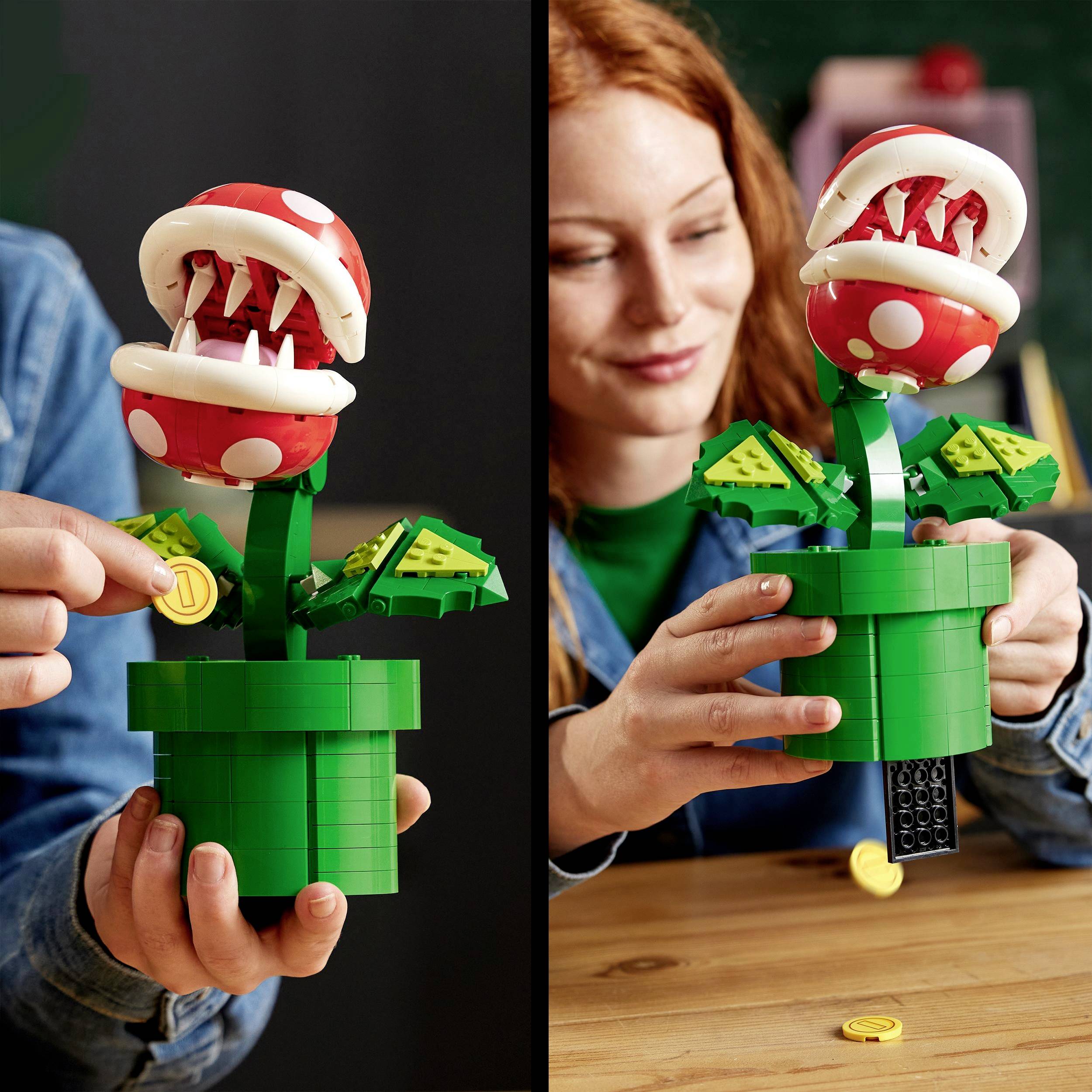 Eine Person hält ein Lego-Modell einer Pflanzenfigur mit großen Zähnen und roten Köpfen in einem grünen Rohr.