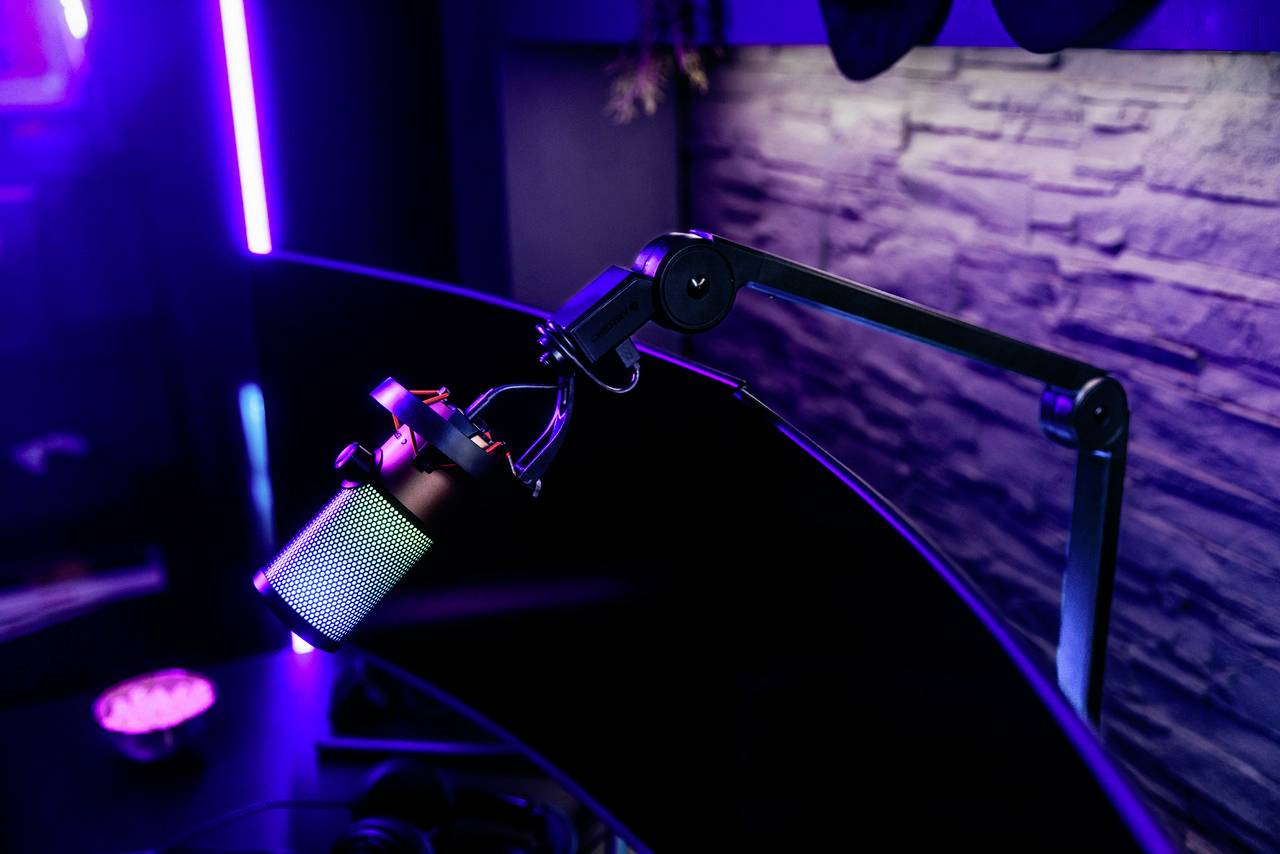 Ein modernes Studiomikrofon an einem Schwenkarm, beleuchtet von blauem und violettem Licht, in einem professionellen Aufnahmeumfeld.