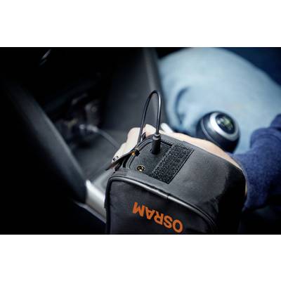 Eine Person im Auto lädt ein Gerät in einer Tasche mit 'OSRAM'-Aufschrift über eine Steckverbindung auf. Im Hintergrund ist der Schaltknauf sichtbar.