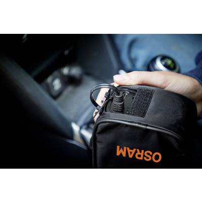Eine Person hält eine schwarze Tasche mit der Aufschrift 'OSRAM', in die ein Ladekabel eingesteckt wird, im Inneren eines Fahrzeugs.