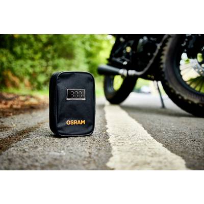 Eine schwarze Tasche mit dem Aufdruck 'OSRAM' steht auf einer Straße neben einem Motorradreifen. Im Hintergrund ist grüne Vegetation sichtbar.