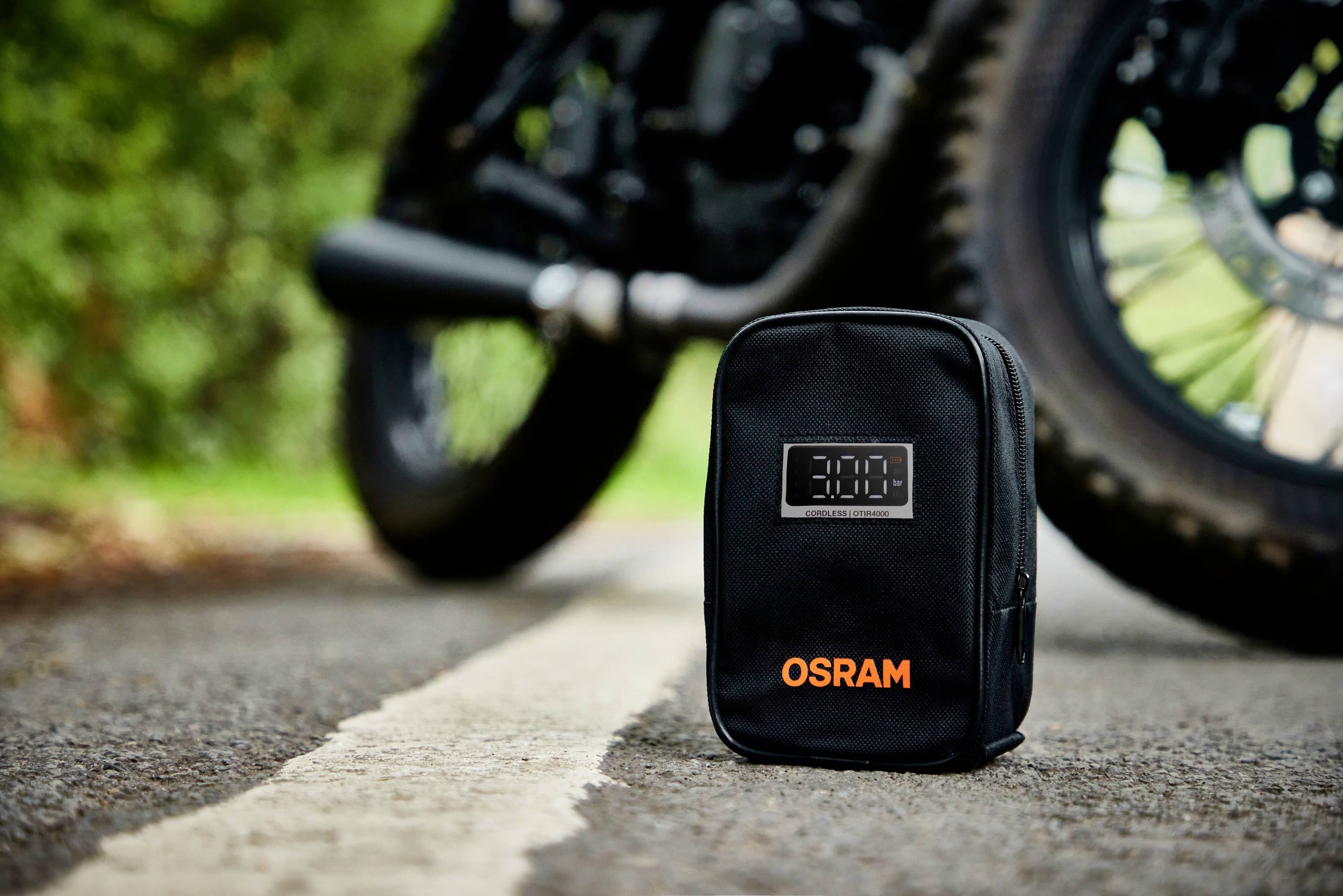 Eine schwarze OSRAM-Tasche liegt auf einer Straße vor einem Motorrad.