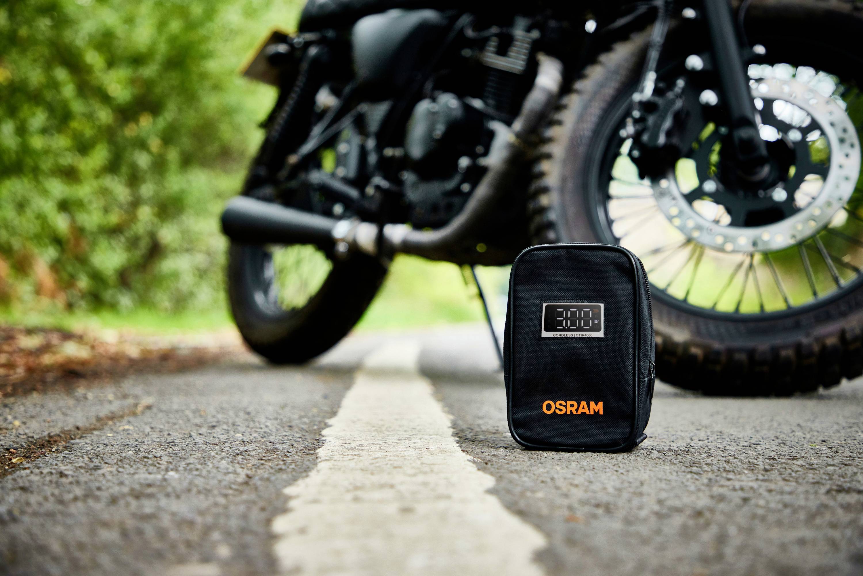 'OSRAM'-Tasche liegt auf einer Straße im Fokus, im Hintergrund ein Motorrad.