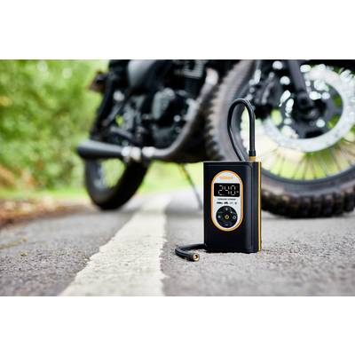 Ein tragbarer Reifenkompressor zeigt '2.40' an, steht auf einer Straße vor einem Motorrad.