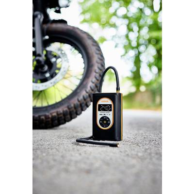 Tragbarer Reifendruckmesser auf Asphalt neben Motorradreifen, im Freien vor Bäumen.