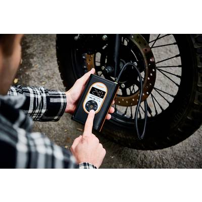 Eine Person überprüft den Reifendruck eines Motorrads mit einem digitalen Druckmessgerät. Das Display zeigt '2.40'.