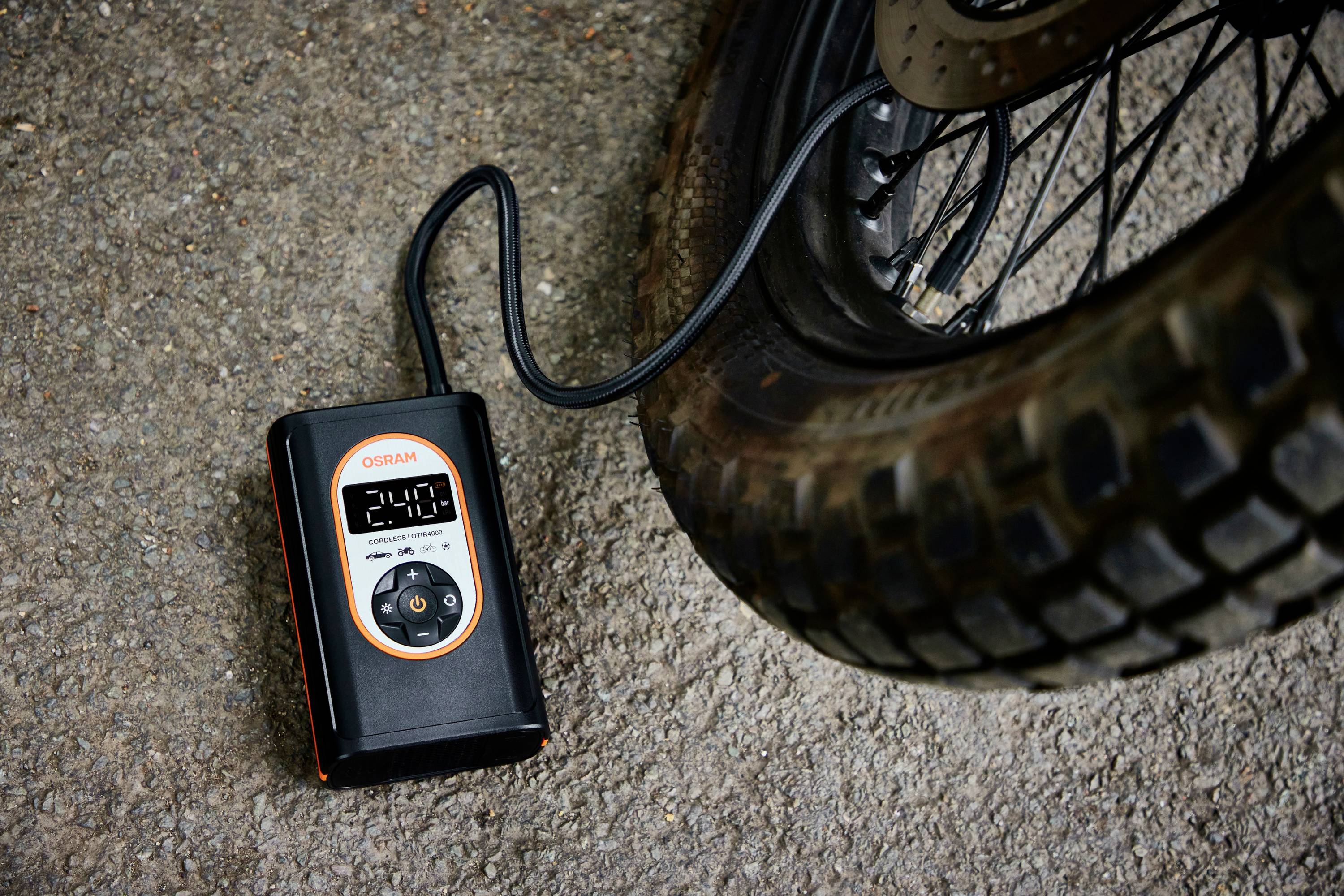 Ein schwarzer tragbarer Kompressor pumpt einen Autoreifen auf. Das Display zeigt '2.41', verbunden mit dem Reifen über ein Schlauchventil.