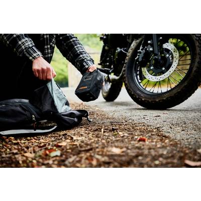 Eine Person packt Rucksack neben einem Motorrad aus, das auf einem Waldweg steht. Fokus auf Hände und Motorradreifen.