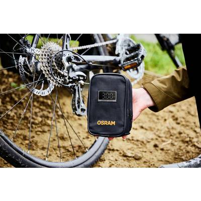 Eine Person hält eine schwarze Tasche mit der Aufschrift "OSRAM" neben einem Fahrrad. Das Fahrrad zeigt Zahnräder und eine Disc-Bremse.