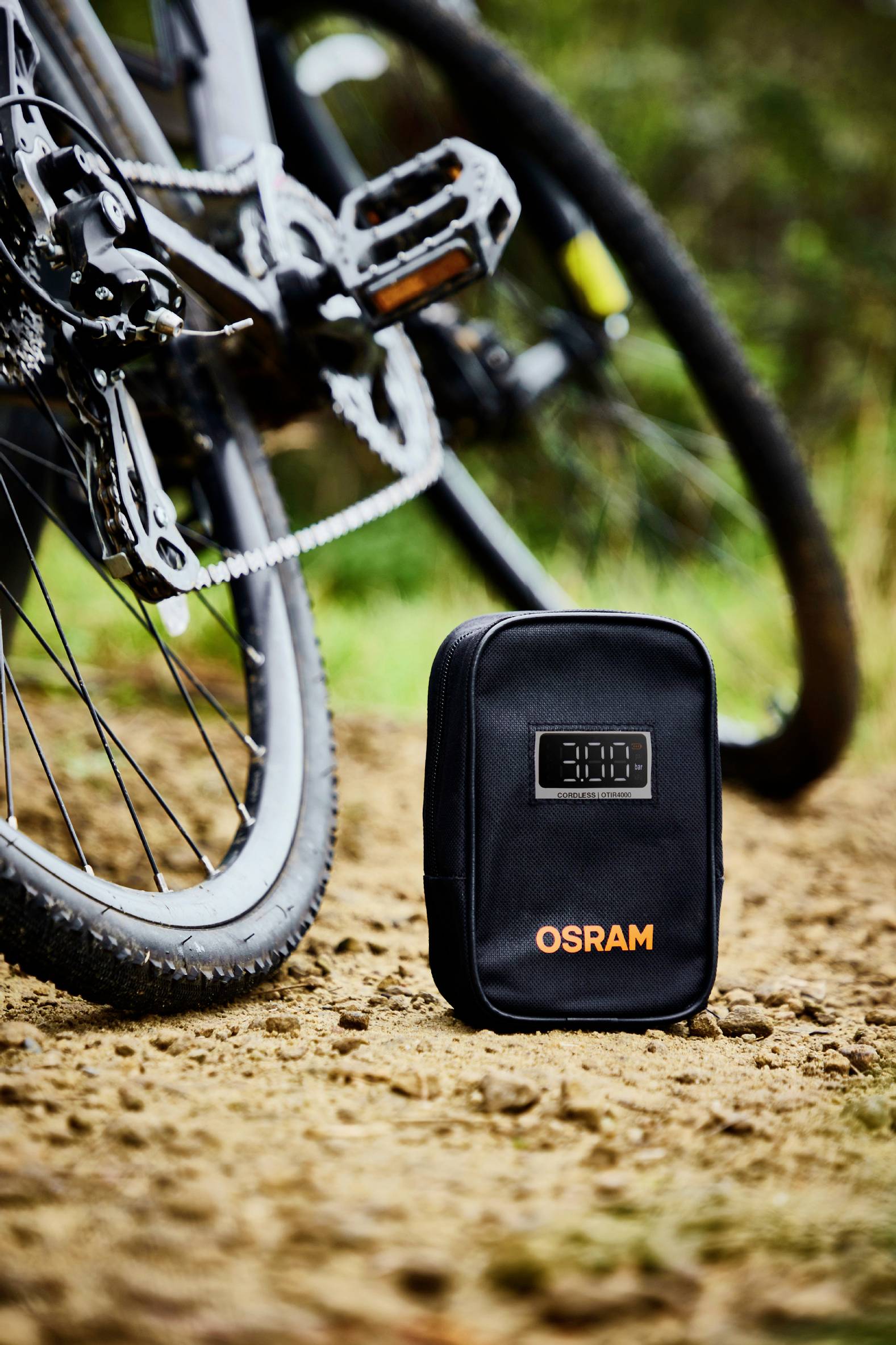 'OSRAM' schwarze Fahrradtasche mit digitaler Anzeige steht auf einem Waldweg neben einem Fahrrad.