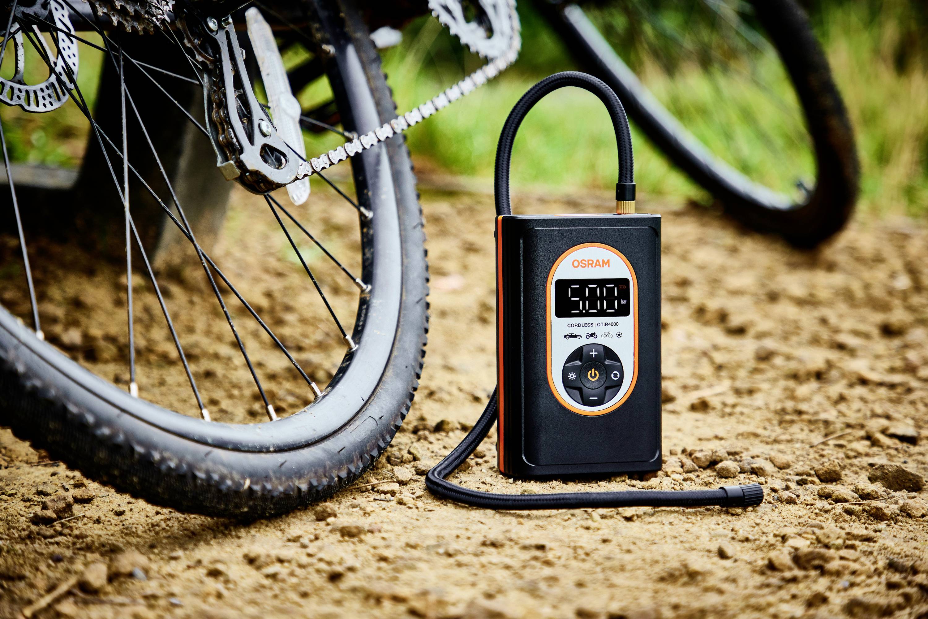 Luftkompressoranhänger auf schlammigem Boden bei Fahrrad. Zeigt 5,0 auf Display, mit Schlauch angeschlossen. Ideal für Fahrradreifenaufpumpen.