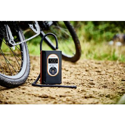 Ein elektrischer Luftkompressor steht auf einem unbefestigten Weg neben einem Fahrrad, bereit zum Aufpumpen der Reifen.
