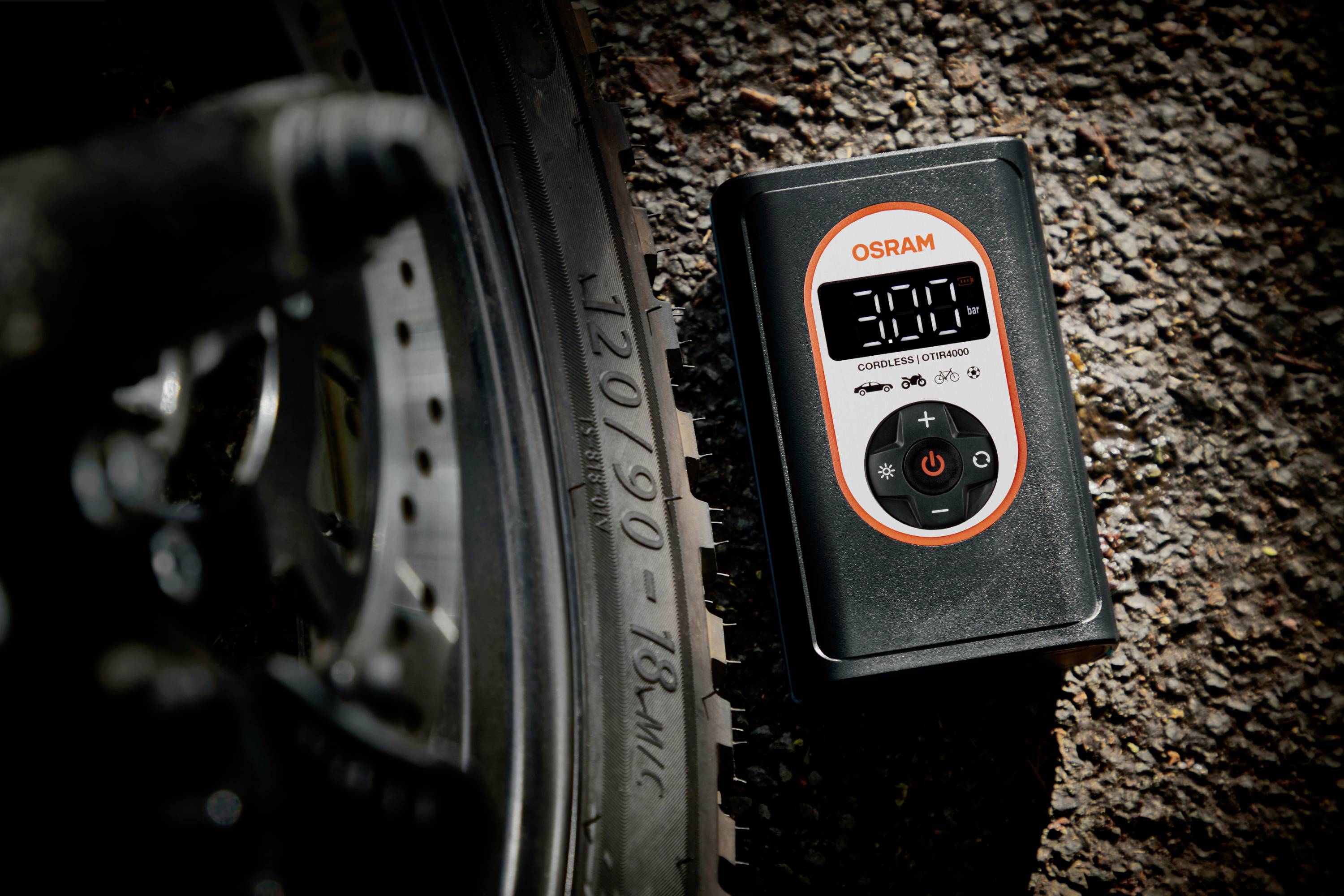 Ein elektronischer Luftdruckmesser zeigt '3.00' neben einem Fahrradreifen auf einer Asphaltstraße an. Das Logo 'OSRAM' ist sichtbar.