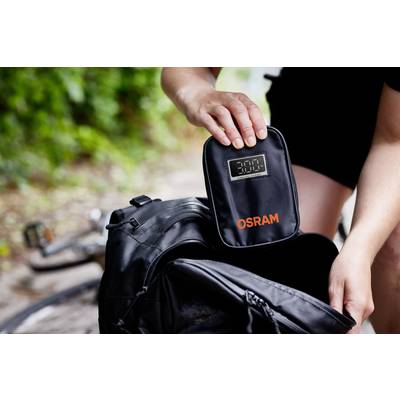 Eine Person packt eine kleine schwarze Tasche mit der Aufschrift 'OSRAM' in einen Rucksack. Im Hintergrund ist ein Fahrrad sichtbar.
