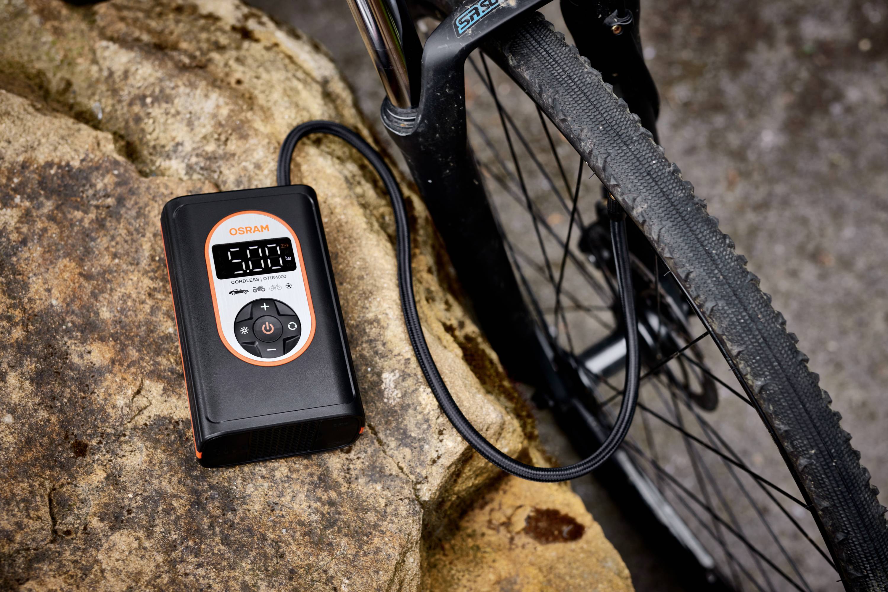 Ein digitaler Reifenfüller neben einem Fahrradreifen zeigt den Reifendruck von 5,00 bar an, platziert auf einem Felsen.